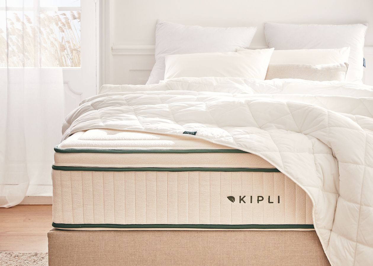 A Kipli natural latex mattress with a white comforter and pillows, showcasing healthy and sustainable bedding in a bright bedroom.