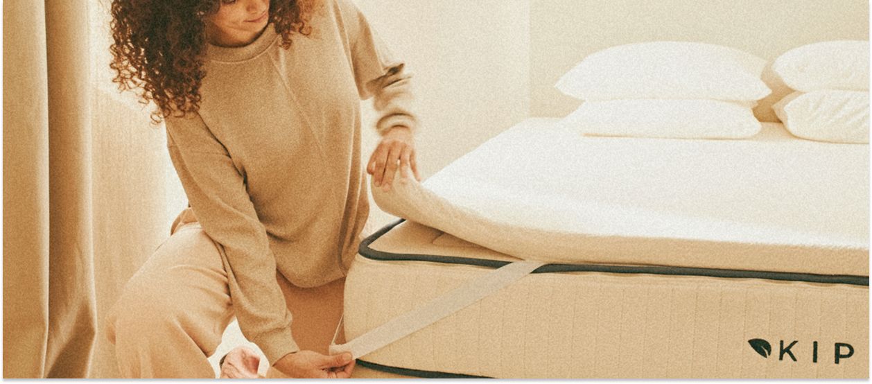 En kvinde lægger en topmadras på en Kipli-madras af naturlatex i et lyst og minimalistisk soveværelse.