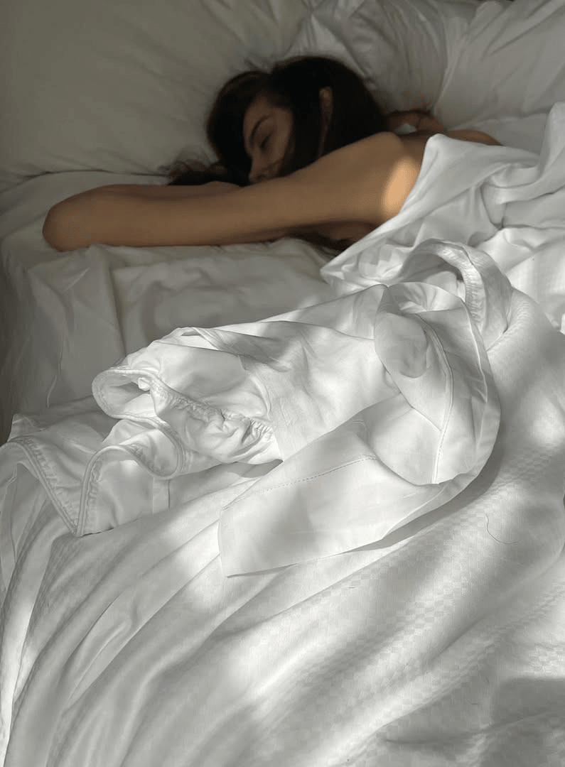 Personne endormie dans des draps blancs baignés de lumière naturelle, illustrant un sommeil réparateur et une literie confortable et apaisante.