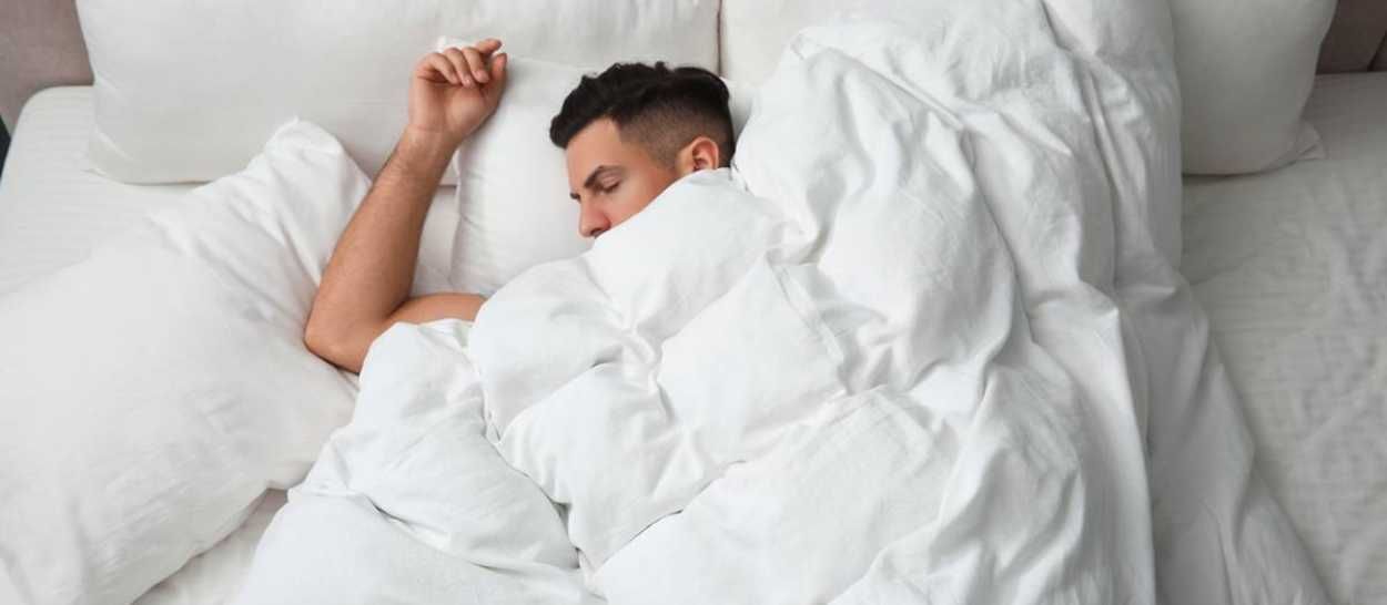 En mand, der sover dybt i en blød seng, hvilket illustrerer behovet for at sove længere om vinteren.