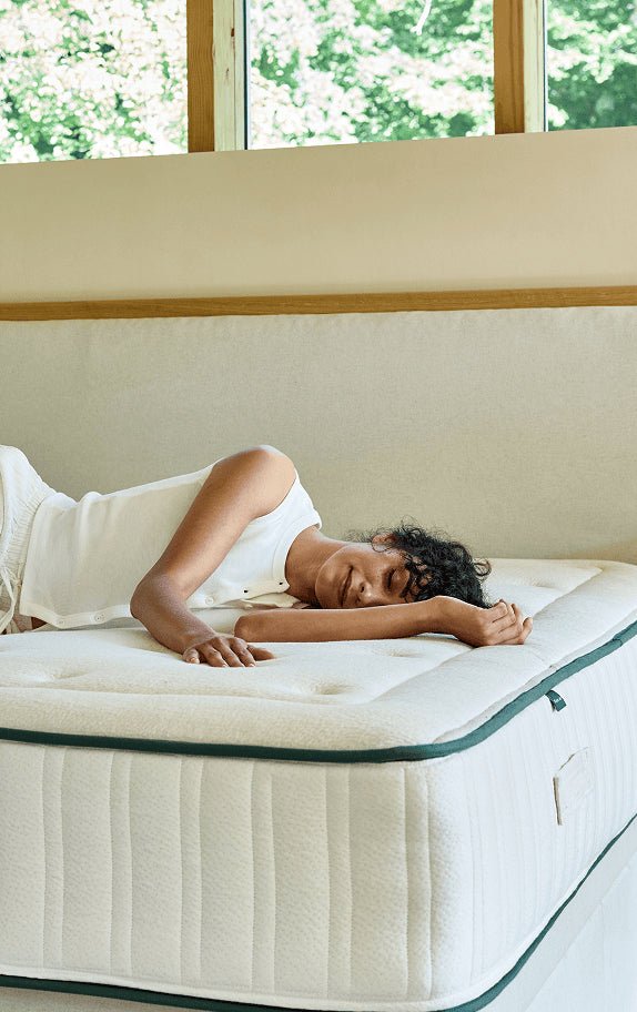 A woman lying on a Kipli natural latex mattress in a bright bedroom, illustrating the comfort and support provided by this eco-friendly mattress.