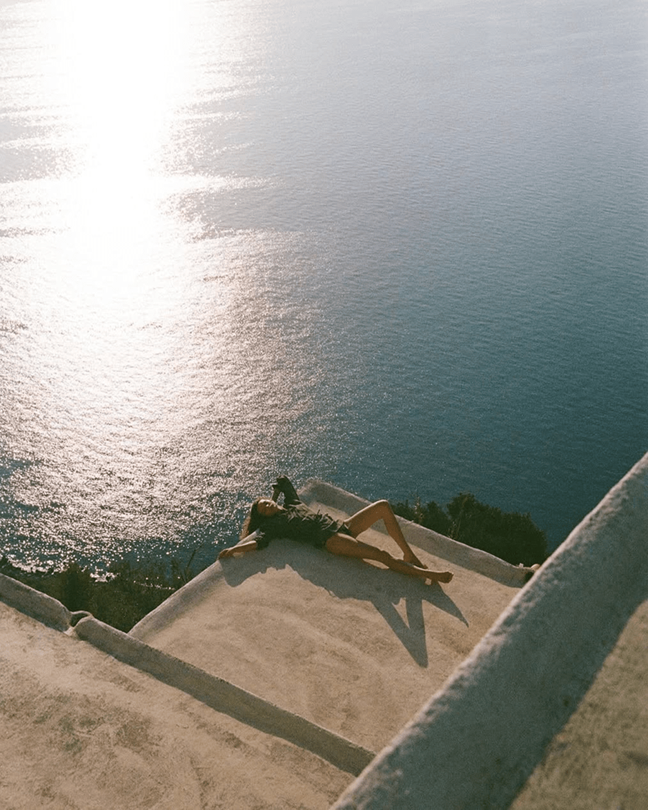 Donna sdraiata al sole di fronte al mare, che raffigura un momento di relax e benessere immersi nella natura, simbolo di uno stile di vita sereno e rigenerante.